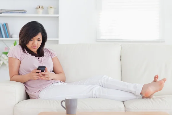 Frau liegt auf einer Couch, während sie ein Telefon hält — Stockfoto