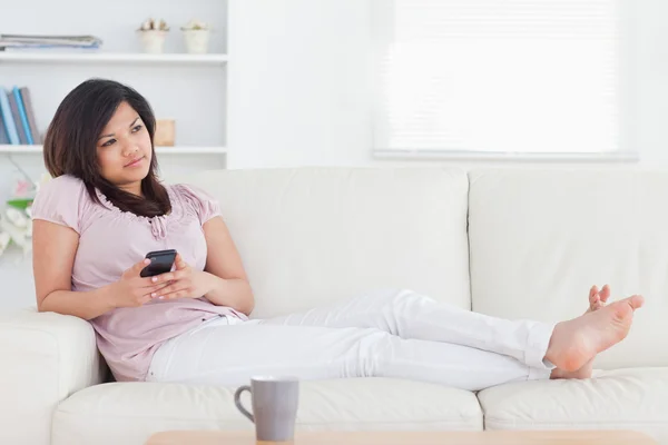 Yalınayak kadın kanepede yatan bir telefon tutarak — Stok fotoğraf