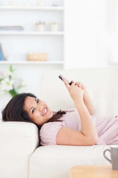 Žena odpočívá na gauči, zatímco drží telefon — Stock fotografie
