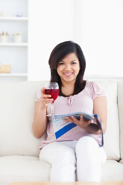 Frau blickt voraus, während sie eine Zeitschrift liest und ein Glas Wein in der Hand hält — Stockfoto