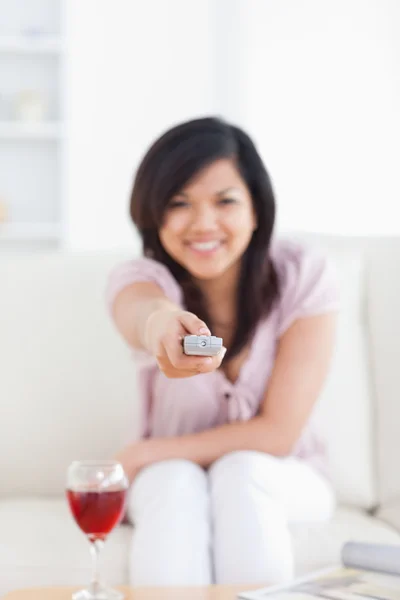 Verschwommene Frau hält eine Fernbedienung in der Hand, während sie auf einer Couch sitzt — Stockfoto