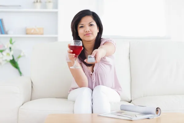 Woman holds a glass of wine and a television remote — Stock Photo, Image