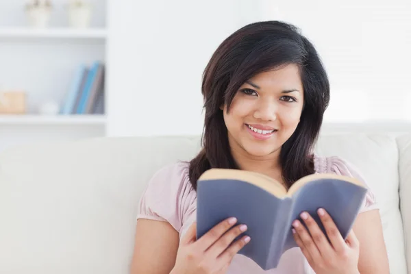 Donna seduta su un divano mentre tiene un libro — Foto Stock