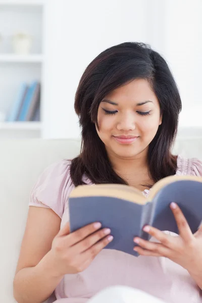 Mujer se sienta en un sofá mientras lee un libro — Foto de Stock