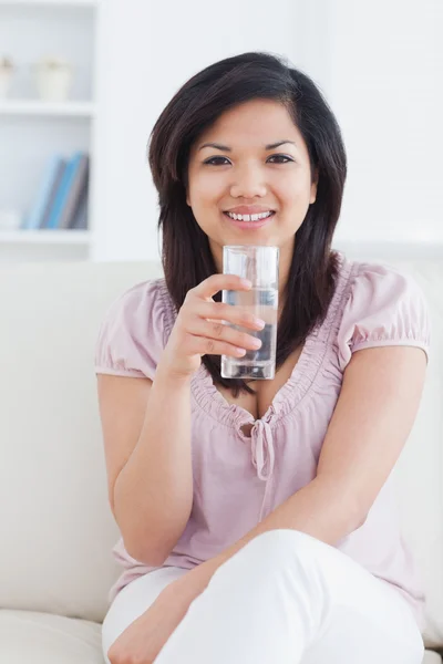 Woman smiling while sitting on a couch and holding a glass of wa — Stock Photo, Image