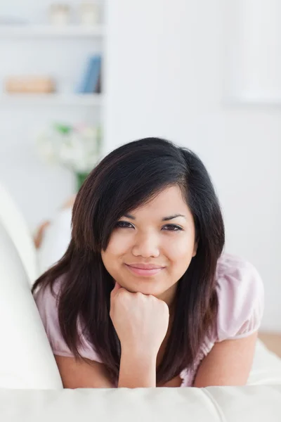 Lächelnde Frau, die auf einer Couch liegt, während sie ihren Kopf mit ihrem — Stockfoto