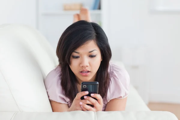 Überraschte Frau blickt auf ein Telefon auf dem Sofa — Stockfoto