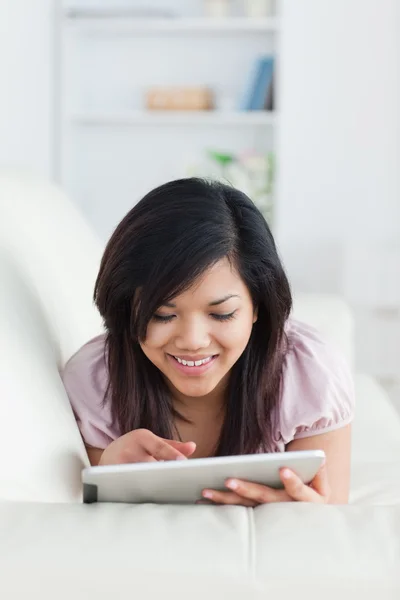 Mujer sonriente descansando en un sofá mientras juega con una tableta — Foto de Stock