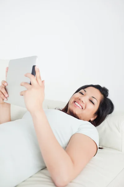 Lachende vrouw liggen op een bank terwijl een tactiele tablet — Stockfoto