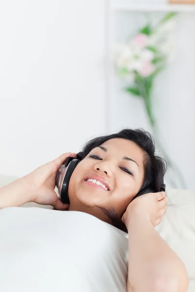 Mulher sorrindo e deitada em um sofá com fones de ouvido em — Fotografia de Stock