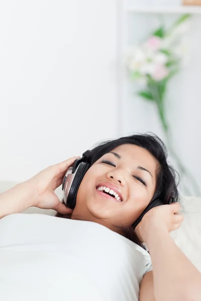 Χαμογελώντας γυναίκα ξαπλωμένη σε έναν καναπέ με τα ακουστικά για — Φωτογραφία Αρχείου