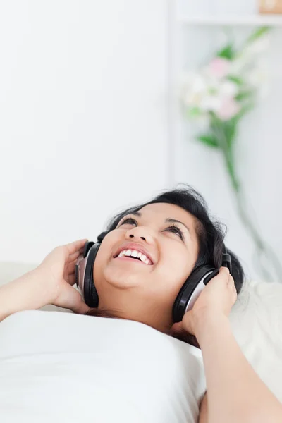Sorrindo mulher deitada em um sofá com fones de ouvido em — Fotografia de Stock