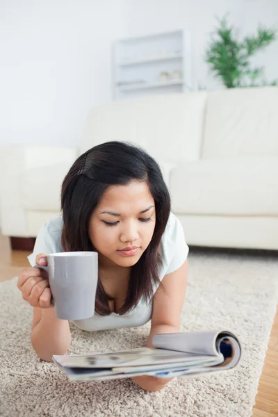 Mujer sosteniendo una taza mientras lee una revista en el suelo —  Fotos de Stock