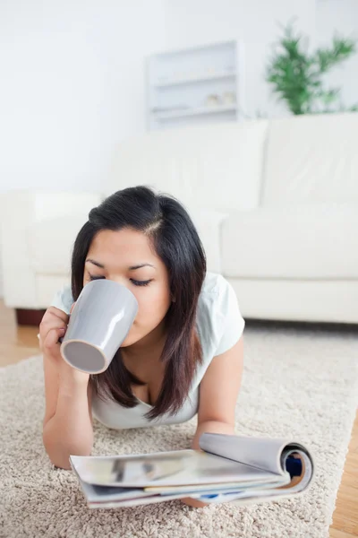 Donna che beve da una tazza mentre tiene in mano una rivista — Foto Stock