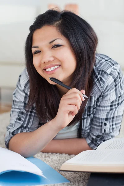 Mujer sonriente sosteniendo una pluma mientras yace en el suelo — Foto de Stock