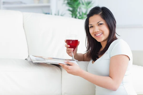 Žena na kolena drží sklenici červeného vína a časopis — Stock fotografie