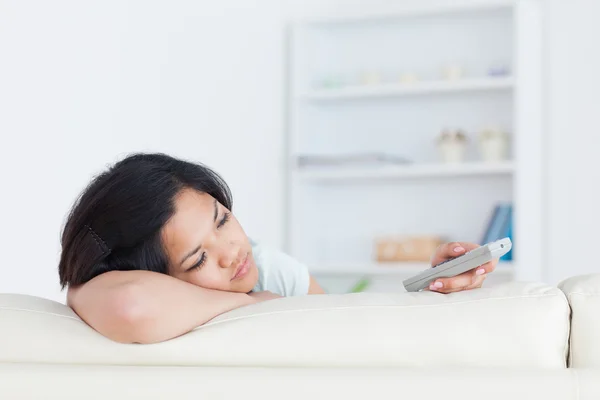 Mujer con un control remoto en la mano apoyando la cabeza en un couc blanco — Foto de Stock