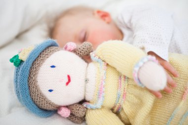 Baby sleeping while holding a plush doll clipart