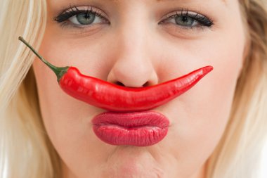 Cheerful woman placing a chili between her nose and her mouth clipart