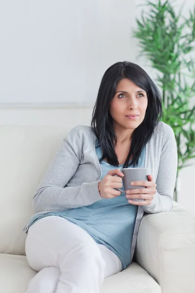 Woman sitting on a couch while crossing her legs and holding a m — Stock Photo, Image