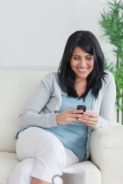 Žena uvolňující na pohovce, zatímco drží telefon — Stock fotografie