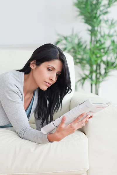 女人在沙发上放松的同时阅读一本杂志 — 图库照片