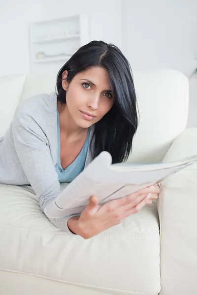 Vrouw op een bank te leggen zoals ze een tijdschrift houdt — Stockfoto