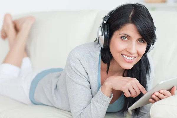 Donna sorridente con le cuffie mentre tiene in mano un tablet — Foto Stock