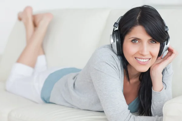 Mulher sorrindo com fones de ouvido enquanto deitada em um sofá — Fotografia de Stock