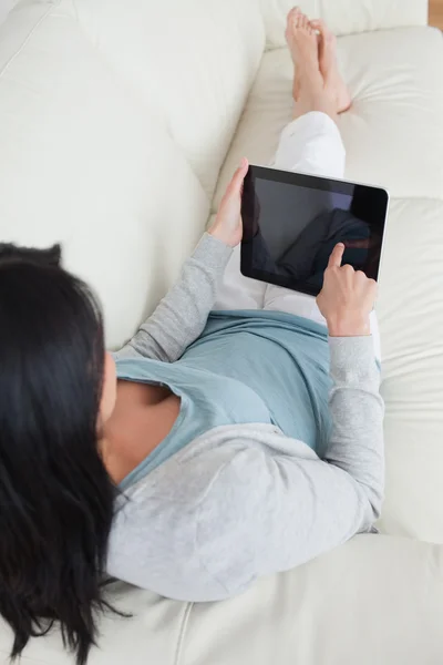 Frau liegt auf Sofa, während sie ein taktiles Tablet berührt — Stockfoto