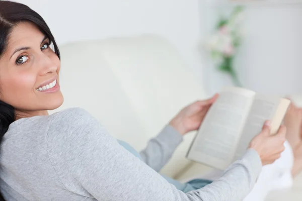 Donna che tiene un libro mentre si trova su un divano — Foto Stock