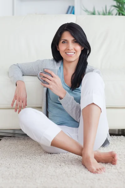 Kobieta siedzi na podłodze trzymając kubek — Zdjęcie stockowe