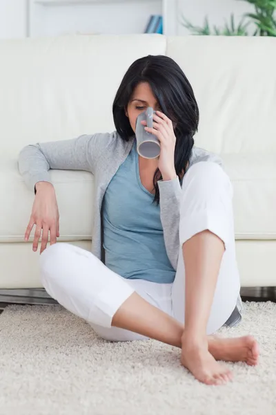 Mujer sentada en el suelo mientras bebe de una taza — Foto de Stock