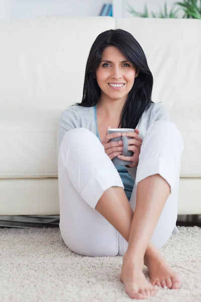 Woman holding a mug with two hands and crossing her legs while s — Stock Photo, Image