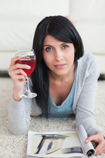 Mulher deitada no chão, segurando um copo de vinho e uma mag — Fotografia de Stock
