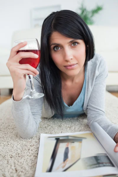 Mulher com uma revista segurando um copo de vinho tinto — Fotografia de Stock