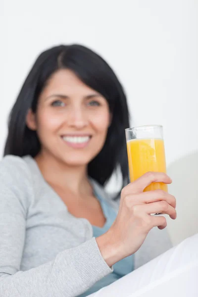 Женщина улыбается, держа стакан апельсинового сока — стоковое фото