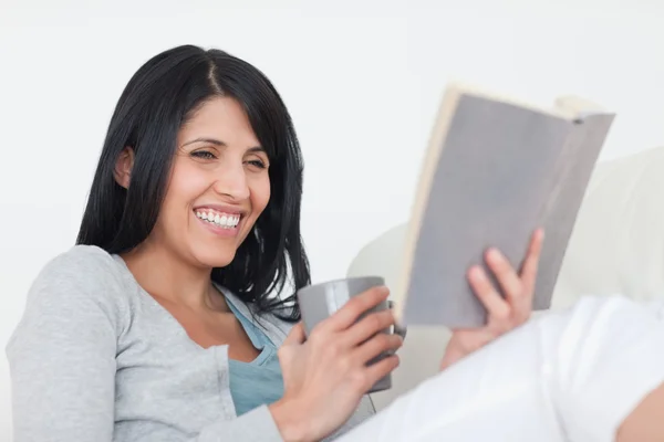 Mulher sorrindo enquanto segura uma caneca cinza e um livro — Fotografia de Stock