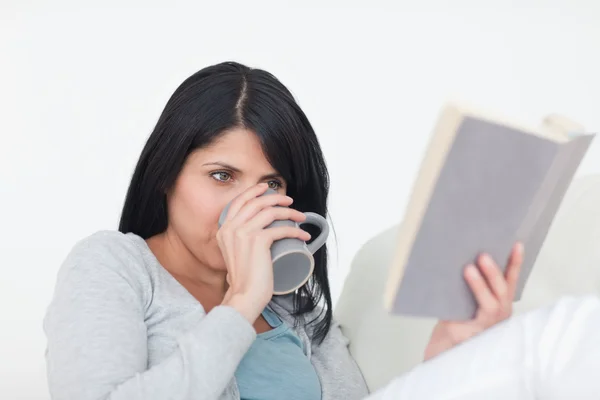 Frau trinkt aus einem grauen Becher, während sie ein Buch liest — Stockfoto