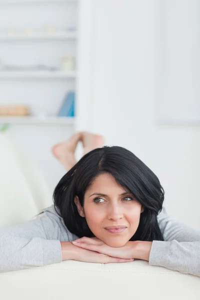 Žena uvolňující na gauči, drží hlavu se dvěma rukama — Stock fotografie