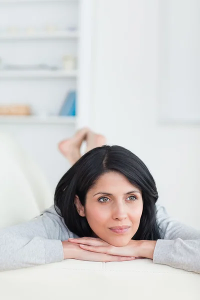 Woman laying on a sofa while holding her head — Stock Photo, Image