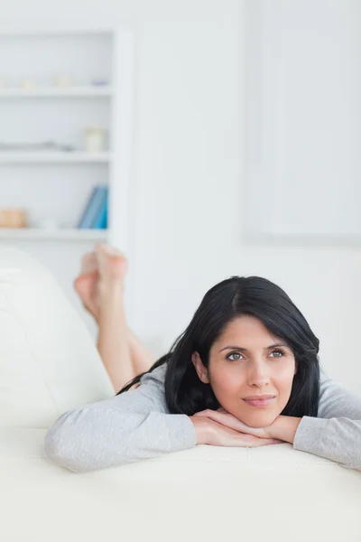 Woman holding her head with two hands while resting on a couch — Stock Photo, Image