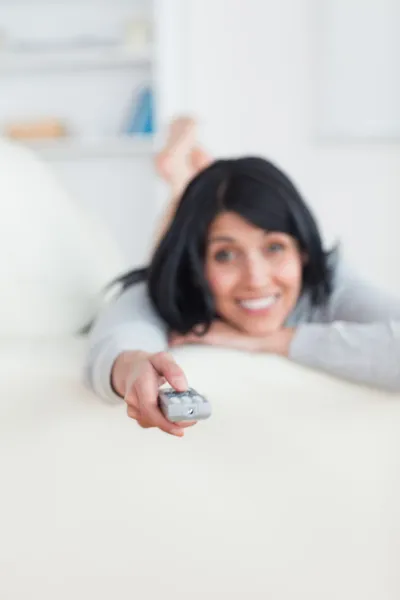 Frau drückt auf Fernbedienung, während sie auf dem Sofa liegt — Stockfoto