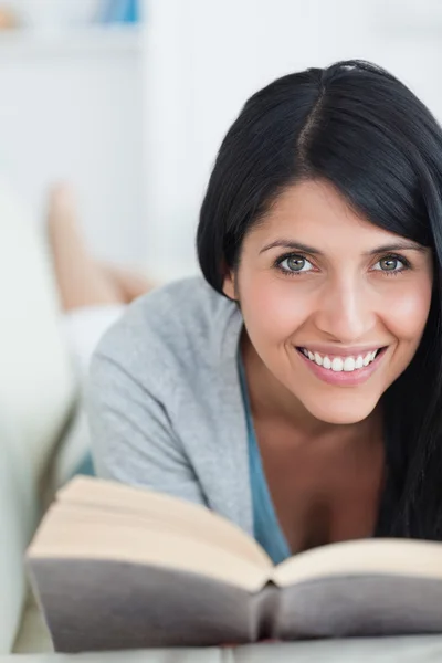 Usmívající se žena čte knihu, jak leží na pohovce — Stock fotografie