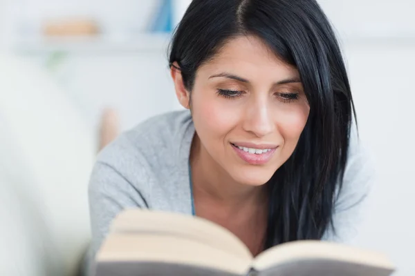 La mujer sonríe mientras sostiene un libro en un sofá — Foto de Stock