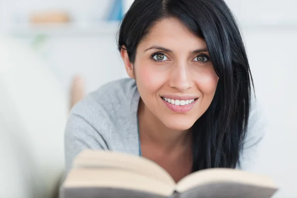 Женщина улыбается, держа книгу в диване — стоковое фото