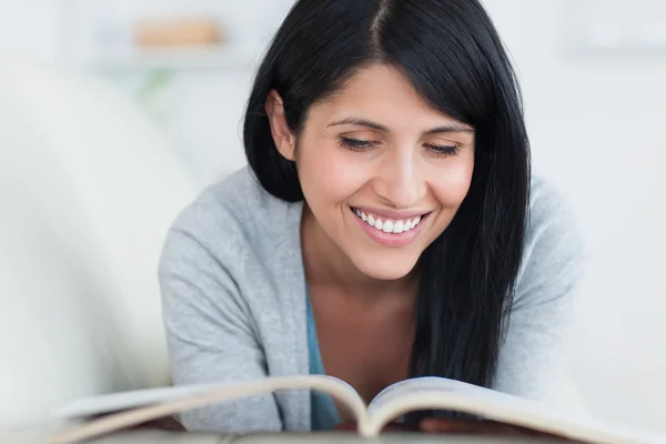 Frau liest ein Buch und lächelt, als sie auf einer Couch liegt — Stockfoto