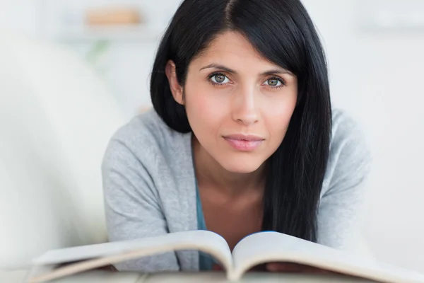 Frau hält ein Buch, während sie sich auf einem Sofa ausruht — Stockfoto