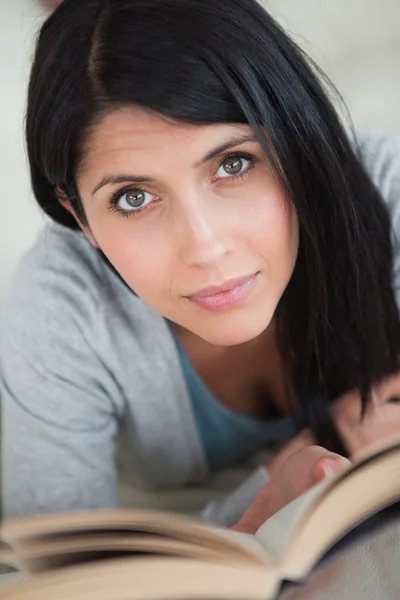 Frau liest ein Buch, während sie auf einem weißen Sofa liegt — Stockfoto