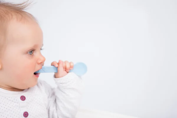 Niedliches Baby beißt in einen blauen Löffel — Stockfoto